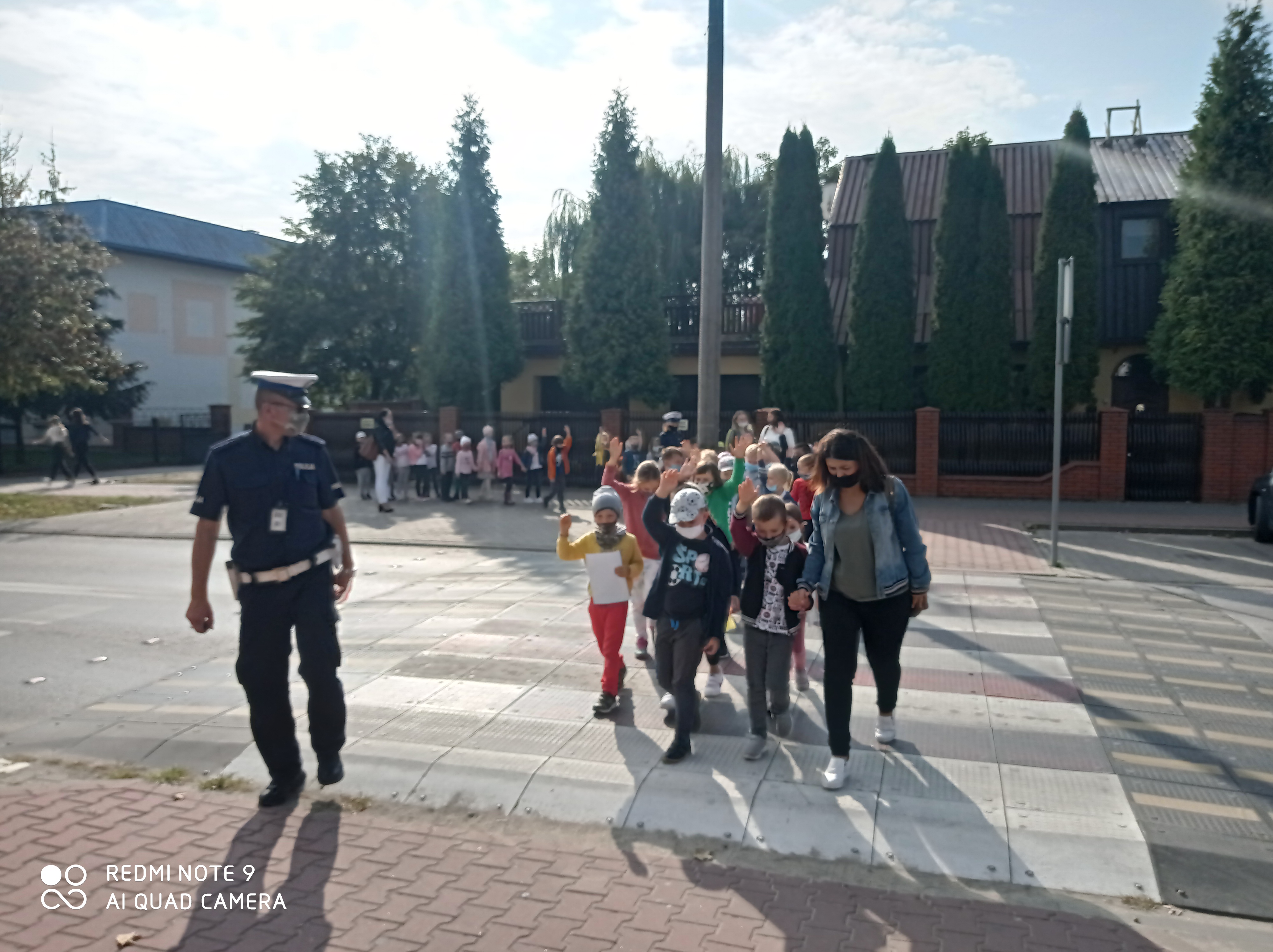Policjant  idzie  z dziecmi oraz nauczyciekami przez przejscie dla pieszych