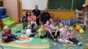 sala przedszkolan dzieci stojące na dywanie  z policjantem
