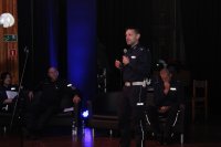 polivcjan opowiada  o  swojej pracy stoi na scenie  w tle uczestnicy spotkania
