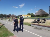 Policjanci patrolujący rejon zalewy w Opocznie. Ida  chodnikiem. W tle widac  parasole oraz ławki i wodę