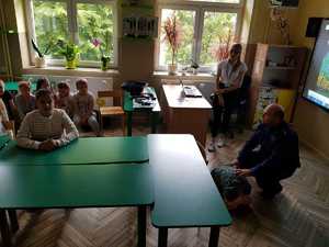 policjant  podczas spotkania w szkole w Januszewicach. Klasa, dzieci siedzą w ławkach, policjant oraz przedstawicielka KRUS rozmawiają z dziećmi.