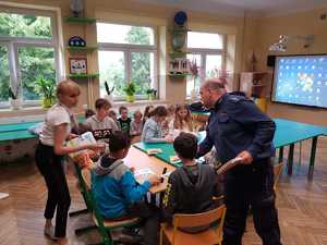 policjant  podczas spotkania w szkole w Januszewicach. Klasa, dzieci siedzą w ławkach, policjant oraz przedstawicielka KRUS rozmawiają z dziećmi.