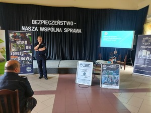 Debata Społeczna w Białaczowie policjanci stoją za nimi napis Bezpieczeństwo nasza wspólna sprawa w tle na krzesłach siedzą mieszkańcy gminy