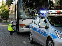 policjant wchodzi do autokaru, z przodu stoi zaparkowany oznakowany radiowóz policji.
