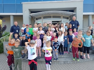 na zdjęciu widać dzieci i dwóch policjantów stojących przed budynkiem Komendy Powiatowej Policji w Opocznie