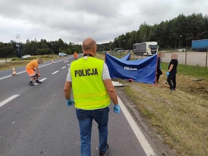 miejsce wypadku drogowego w Grębenicach, policjant idzie do parawanu, w tle radiowóz, na drodze rozstawione parawany policjanci wykonują oględziny miejsca wypadku