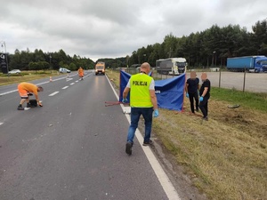 miejsce wypadku drogowego w Grębenicach, policjant idzie do parawanu, w tle radiowóz, na drodze rozstawione parawany policjanci wykonują oględziny miejsca wypadku