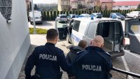 Umundurowani policjanci, prowadzą do radiowozu sprawcę rozboju na 13 letnim chłopcu. Policjanci trzymają mężczyznę pod ręce. w tle widać oznakowany radiowóz policji