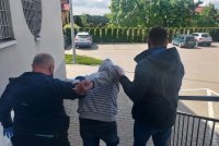 parking komendy, dwaj policjanci prowadzą zatrzymanego mężczyznę do radiowozu