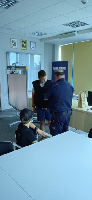 spotkanie policjantów z uczestnikami półkolonii  na terenie KPP w Opocznie. 
Dzieci  rozmawiają z przewodnikiem spa służbowego. Stoją na przeciwko policjanta  który obok ma psa służbowego na smyczy .Kolejne zdjęcia przedstawiają dzieci, które przymierzają elementy wyposażenia policjanta . Policjant stoi tyłem pomaga zakładać dziecku kamizelkę przeciwuderzeniową.Wspólna fotografia z oddali wszystkich uczestników spotkania na tle budynku KPP w Opocznie