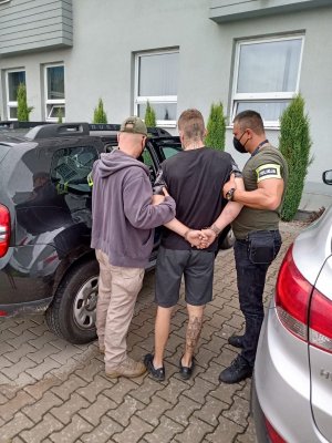 policjanci po cywilnemu prowadzą zatrzymanego, wsiadają do nieoznakowanego radiowozu