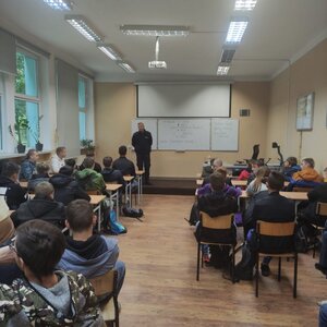 Spotkanie policjantów w szkole. Na foto widać siedzących uczniów, w tle na środku stoi policjant