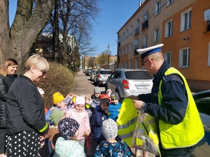 policjant rozdaje elementy odblaskowe  przedszkolakom i rowerzystom,