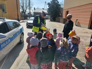 policjant rozdaje elementy odblaskowe  przedszkolakom i rowerzystom,