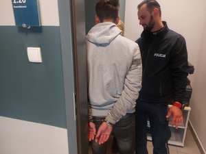 zatrzymany podczas badania stanu trzeźwości, stoi tyłem ręce skute kajdankami, przed nim umundurowany policjant