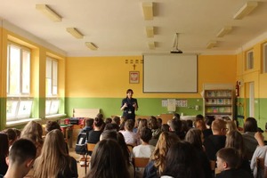 spotkanie z uczniami w Poświętnem.  Uczniowie siedzą w sali na ławkach, przed nimi stoi policjantka.