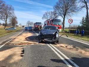 miejsce wypadku drogowego, na drodze stoją policjanci oraz strażacy. widać rozbite samochody. Na miejsce wylądował śmigłowiec pogotowia, w tle obok śmigłowca widać zaparkowane radiowozy policji i straży . Policjanci opisują uszkodzenia pojazdów