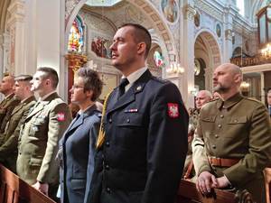 obchody rocznicy zbrodni katyńskiej policjantka składa kwiaty przed pomnikiem. stoi obok umundurowanego strażaka