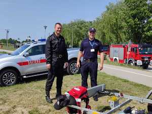 policjant i strażak w kapokach, kaskach na łodzi motorowej, łódź motorowa na zalewie
policjant i strażak stoją obok łodzi na d brzegiem wody