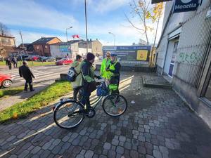 Policjanci wręczają elementy odblaskowe mieszkańcom. Policjantka wręcza odblaski na ulicy rowerzystom, pieszym