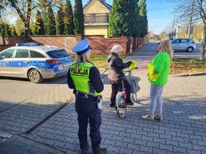 Policjanci wręczają elementy odblaskowe mieszkańcom. Policjantka wręcza odblaski na ulicy rowerzystom, pieszym