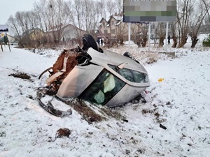 droga, stoją radiowóz i karetka. w polu w rowie leży na dachu rozbity samochód osobowy, Koło radiowozu stoi policjant. w tle strażacy