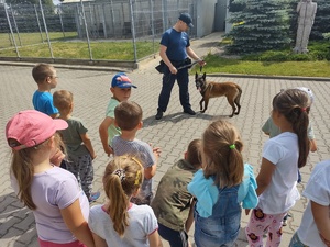 dzieci w komendzie policji, spotkanie z policjantami. Strzelnica policyjna, przewodnik psa służbowego, dzieci stoją policjanci stoją przodem do dzieci, rozmawiają, dzieci przed budynkiem komendy stoją na schodkach