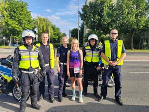 Na zdjęciu policjantka w stroju sportowym, stoi w grupie umundurowanych policjantów.