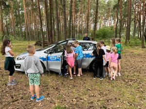 policjant podczas spotkania z zuchami na obozie harcerskim, dzieci stoją wokół policjanta, oglądają radiowóz