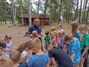 policjant podczas spotkania z zuchami na obozie harcerskim, dzieci stoją wokół policjanta, oglądają radiowóz