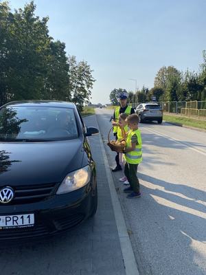 akcja jabłko cytryna.. dzieci i policjanci wręczają kierowcom cytrynę  policjanci stoją obok dzieci  kierowca przyjmuje plaster cytryny