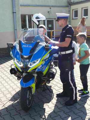 policjanci podczas spotkania z uczniami szkoły. Na placu przed szkoła dzieci stoją wokół policjantów, siedzą za kierownica motocykla policyjnego, wspólne zdjęcie uczniów i policjantów