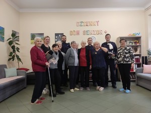 trzech policjantów stoi wśród grupy seniorów.