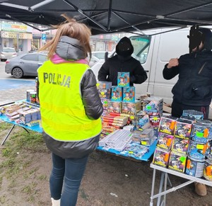 osoba  w kamizelce z napisem policja, stoisko z fajerwerkami.