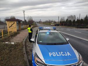 droga , radiowóz, policjantka stoi za radiowozem.