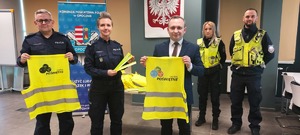 policjanci i mężczyzna w garniturze trzymają elementy odblaskowe, pomieszczenie służbowe policji.