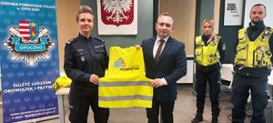 policjanci w mundurach, mężczyzna w garniturze, odblaski, pomieszczenie służbowe policji.