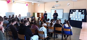 dzieci siedzą na krzesełkach, przed nimi dwóch umundurowanych policjantów.