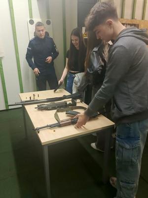 policjant w mundurze, rozmawia z dziećmi, na stole leżą karabiny.