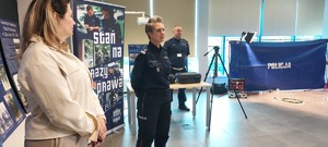 policjantka i policjant w mundurach, bok stoi kobieta w jasnej kurtce. w pomieszczeniu przedmioty do inscenizacji leżą na podłodze
