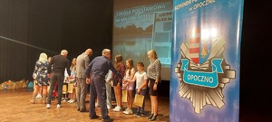 osoby dorosłe, policjant wręczają dzieciom nagrody, napis