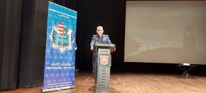policjant stoi przy mównicy, obok niego stoi baner z napisem komenda powiatowa policji w Opocznie.