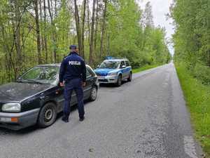droga w lesie, samochód osobowy, przy nim policjant w mundurze, dalej radiowóz policyjny.