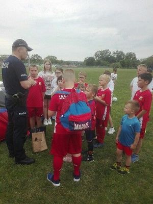 policjant rozmawia z dziećmi w strojach sportowych.