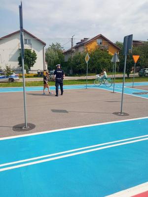policjant rozmawia z dzieckiem, drugie dziecko jedzie rowerem po torze jazdy.