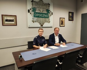 policjantka i mężczyzna podpisują dokumenty, w tle odznaka policyjna, napis Opoczno.