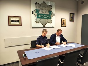 policjantka i mężczyzna podpisują dokumenty, w tle odznaka policyjna napis opoczno.