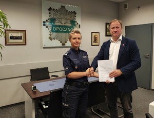 policjantka i mężczyzna podają sobie ręce, trzymają dokument.