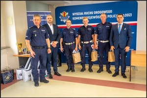 czterech policjantów i dwóch mężczyzn stoi na tle napisu wydział ruchu drogowego.