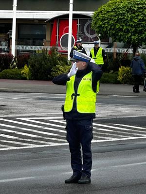 policjant w odblaskowej kamizelce i w białych rękawiczkach stoi na drodze.